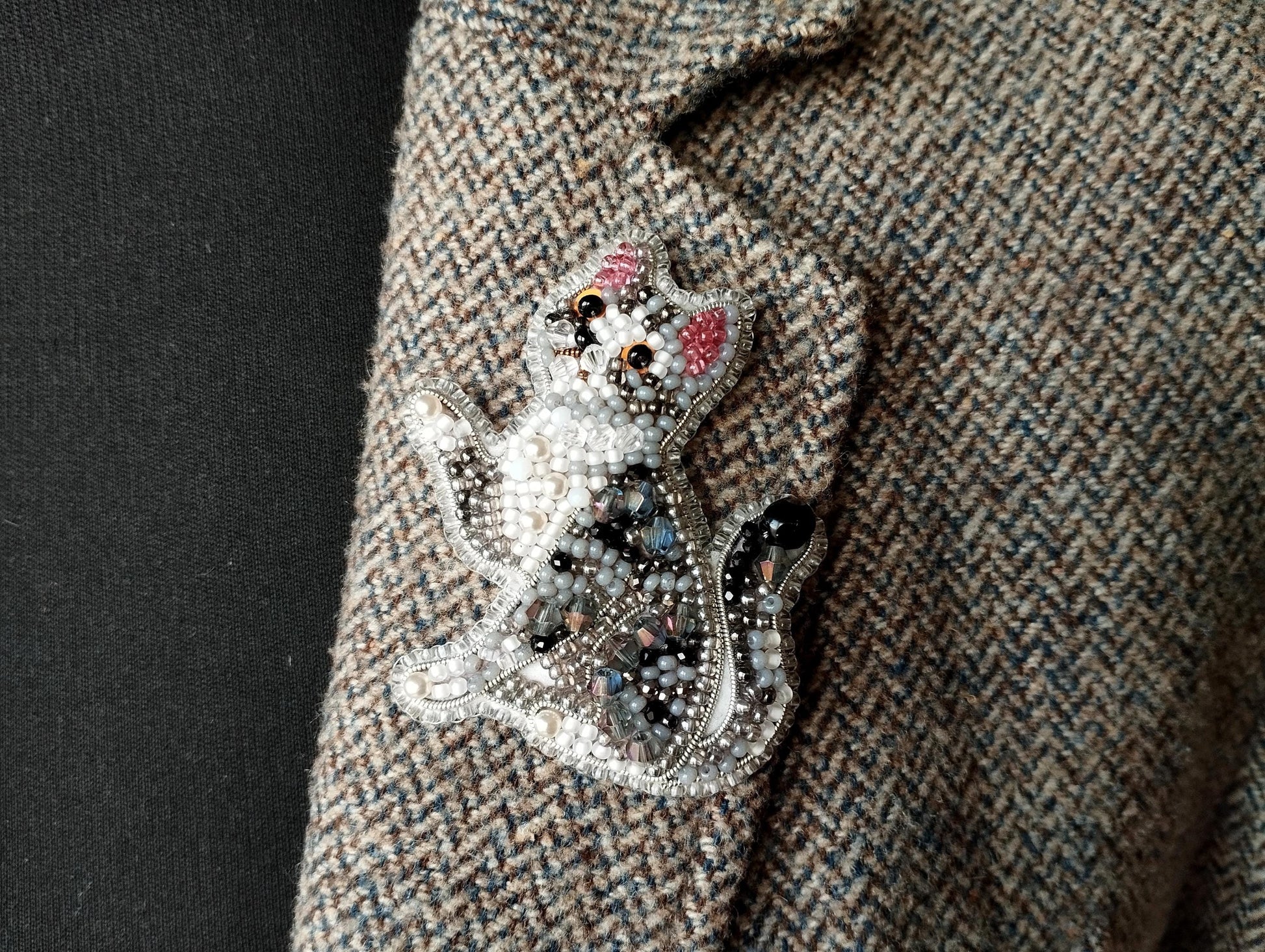 A close-up image of a decorative cat brooch or pin, featuring a detailed and intricate design with various colored beads and embellishments.