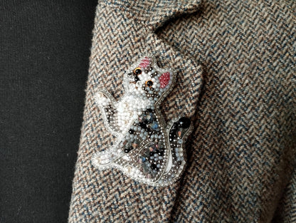 A close-up image of a decorative cat brooch or pin, featuring a detailed and intricate design with various colored beads and embellishments.