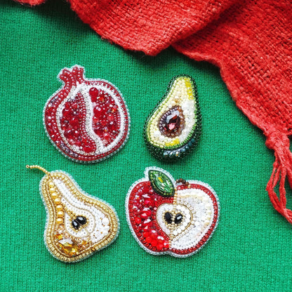 four decorative brooches or pins, each shaped like a different fruit: a pomegranate, an avocado, a pear, and an apple. The fruits are adorned with colorful beads and gemstones, creating a vibrant and eye-catching display.