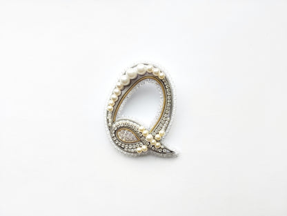 A decorative letter 'Q' made of pearls, diamonds, and other embellishments, displayed against a white background.