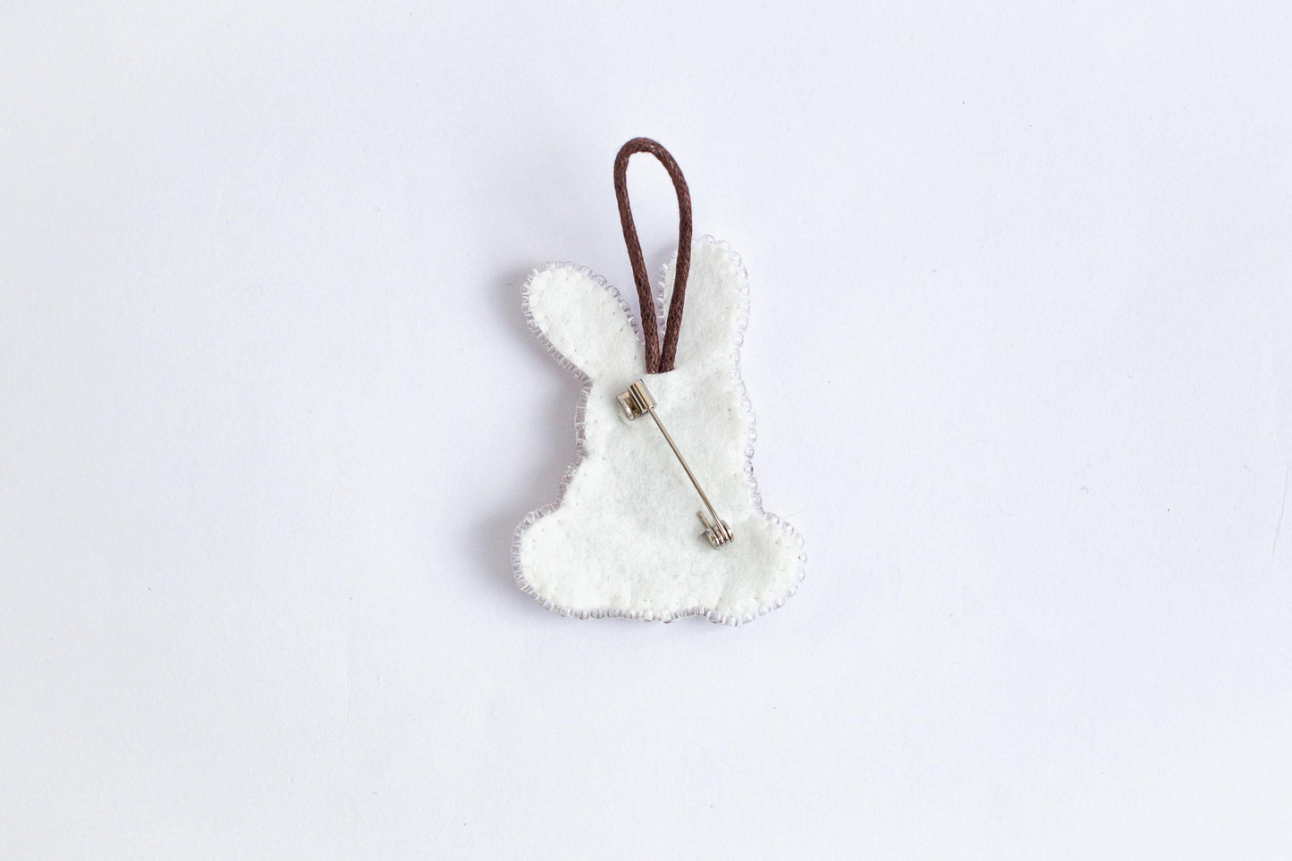 A white felt bunny shape with a brown string attached to it, placed against a plain white background.