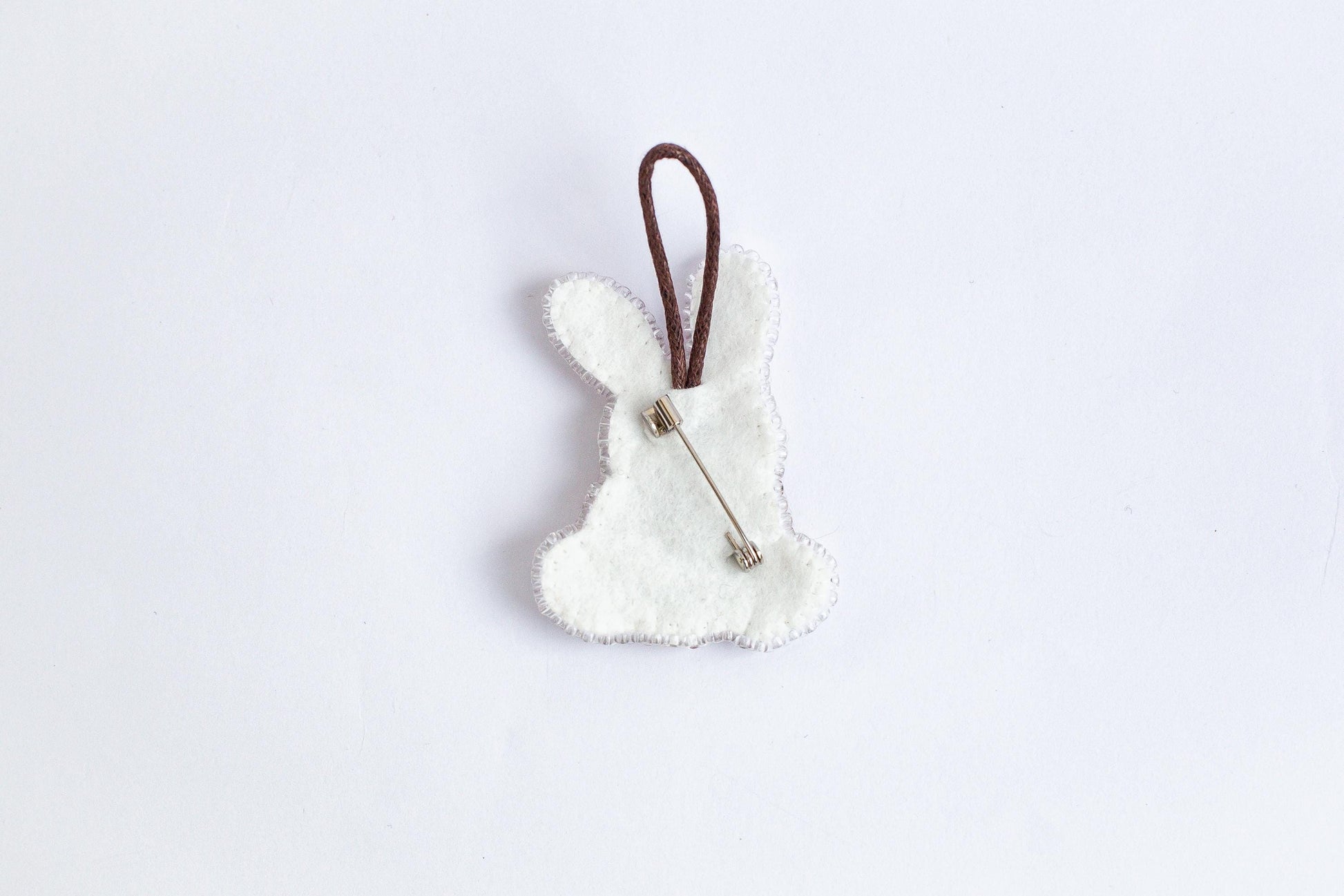 A white felt bunny shape with a brown string attached to it, placed against a plain white background.