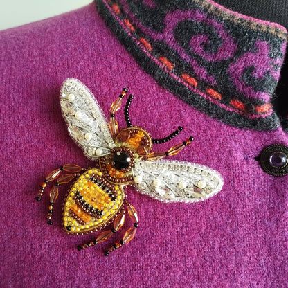 A close-up image of a purple sweater with a detailed, intricately designed beaded bee embroidered on it.