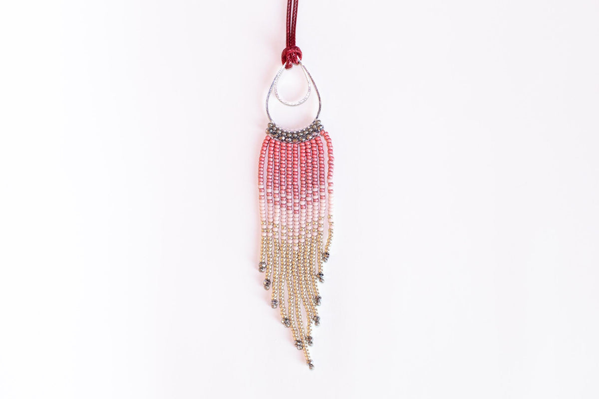 A beaded necklace with a red and silver pendant hanging against a white background.