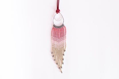 A beaded necklace with a red and silver pendant hanging against a white background.