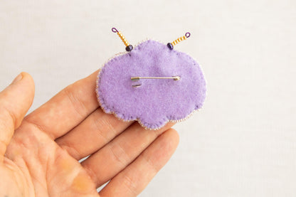 a hand holding a purple pin cushion with a needle