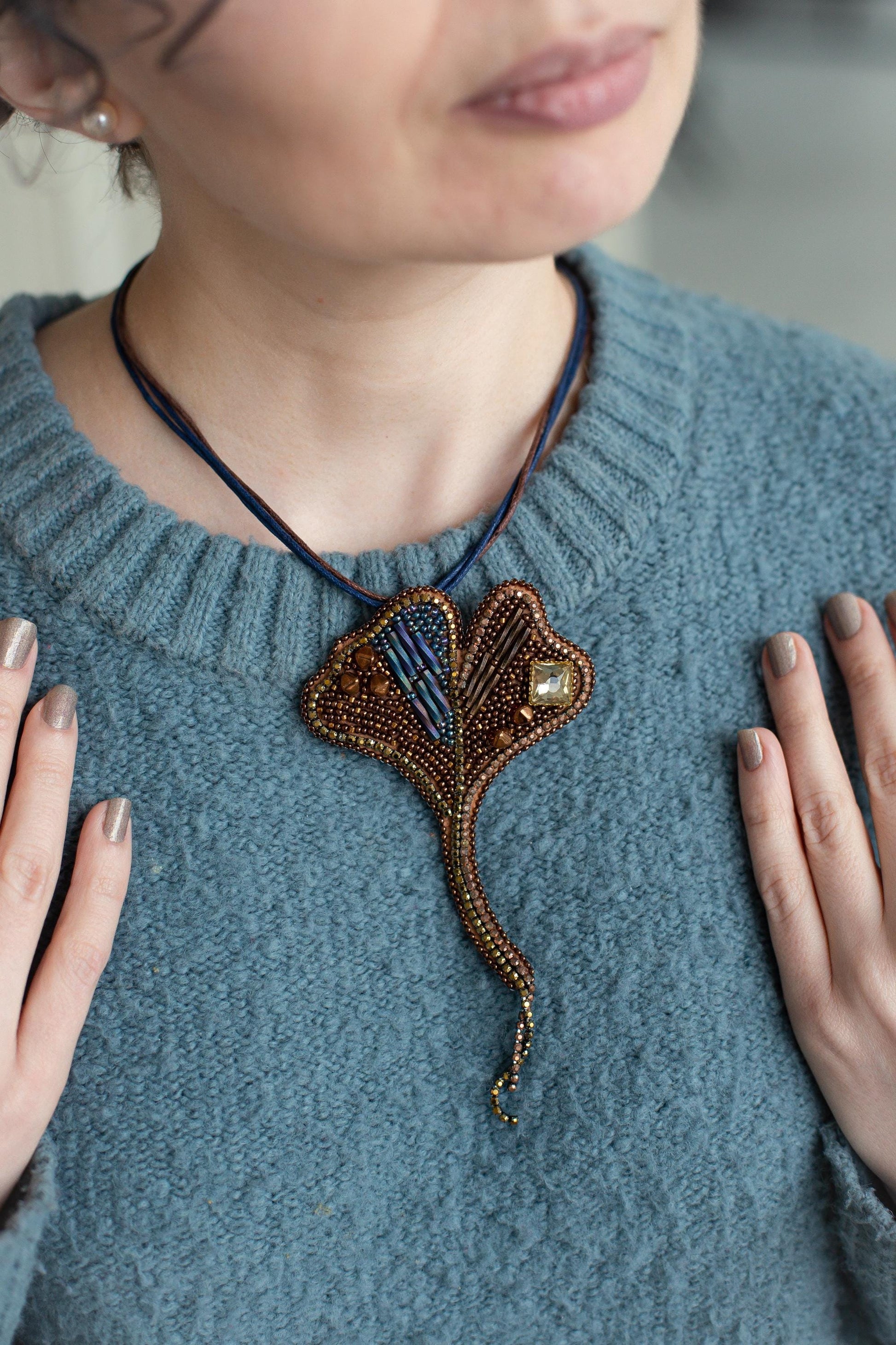 A woman wearing a blue sweater and a necklace with a decorative pendant.