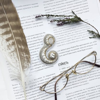 a close-up of a page of text with a pair of glasses, a feather, and a beaded brooch resting on it.