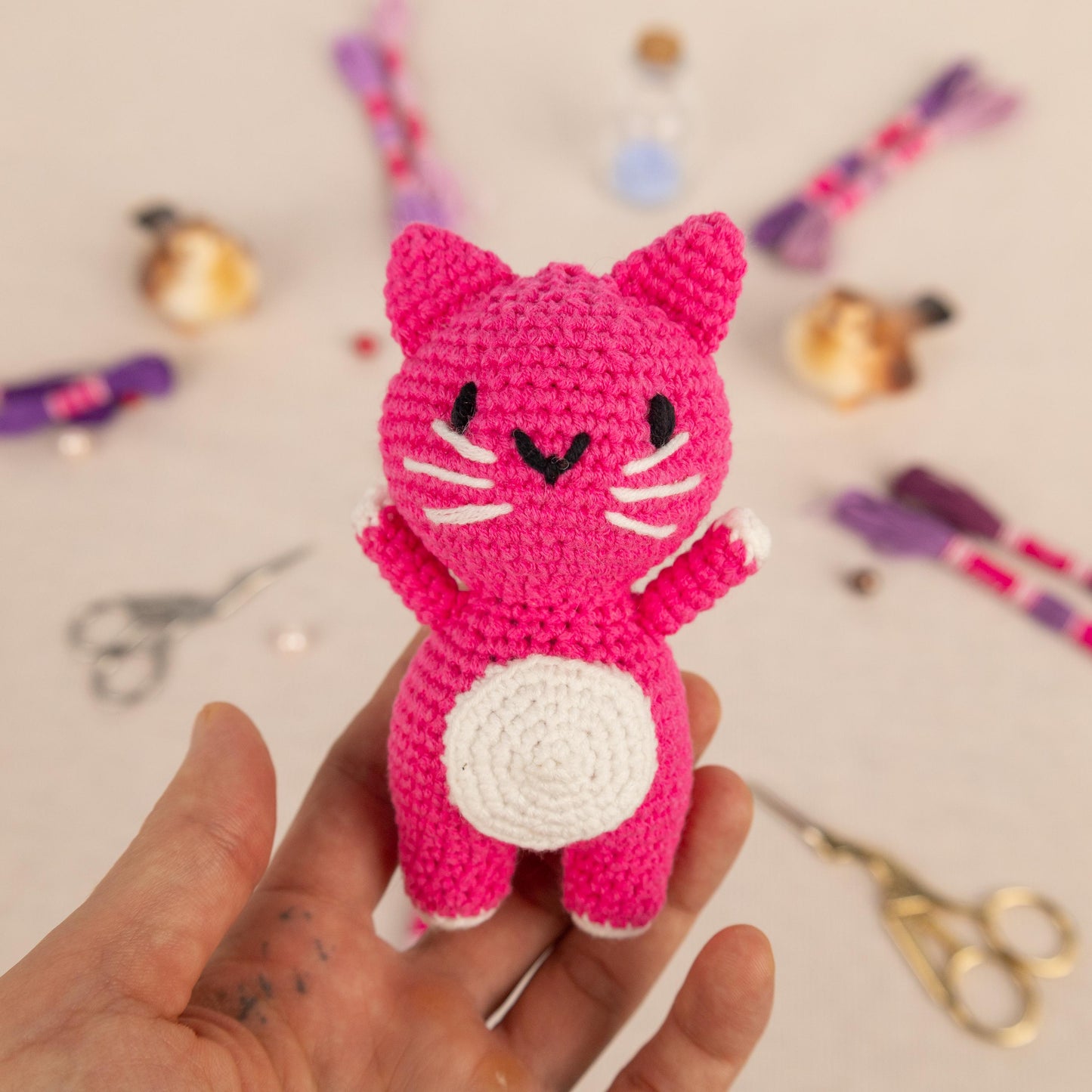 a hand holding a small crocheted pink cat