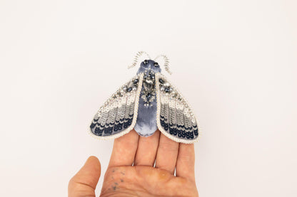 a hand holding a tiny blue and white moth