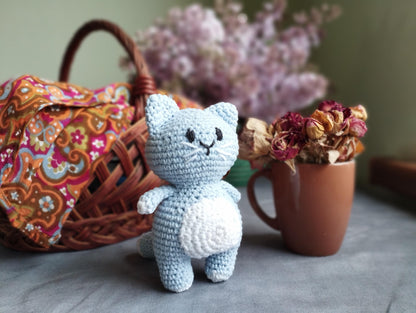 a small crocheted cat sitting next to a basket of flowers