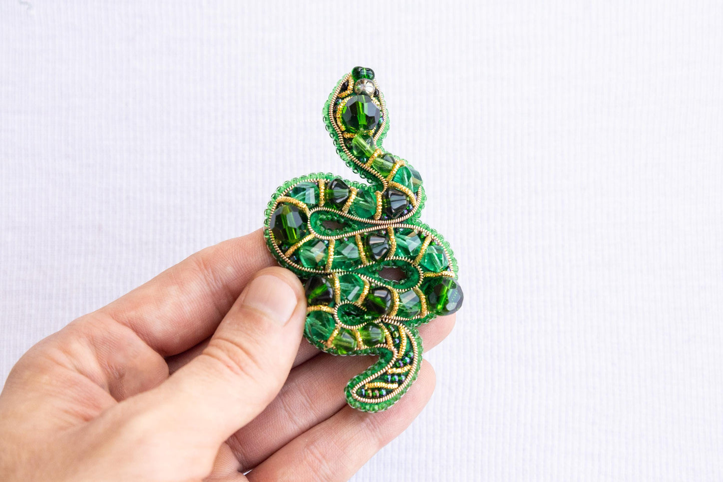 a hand holding a green beaded snake brooch