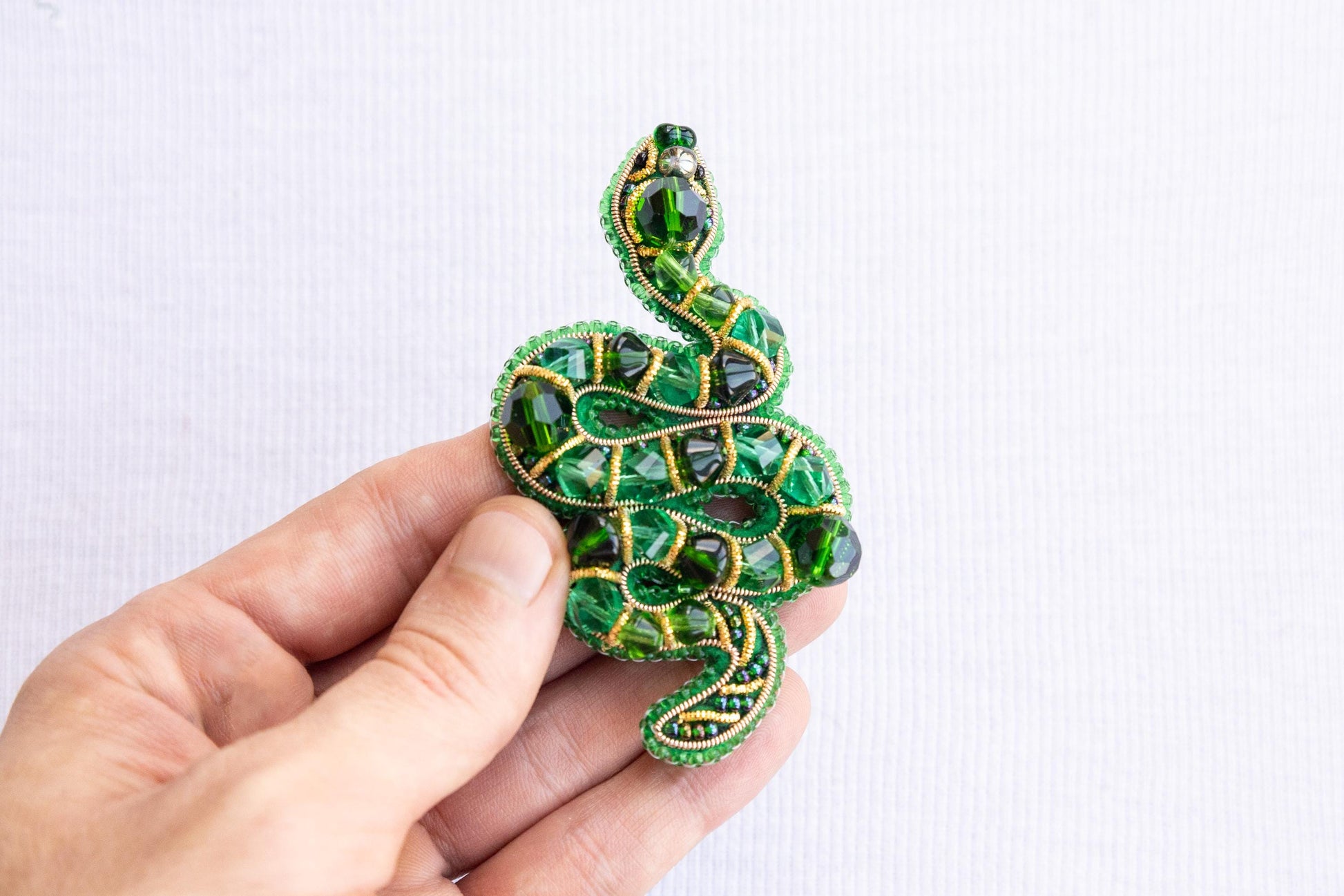 a hand holding a green beaded snake brooch