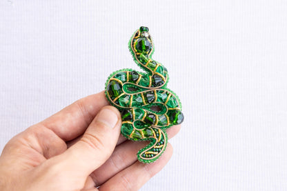 a hand holding a green beaded snake brooch