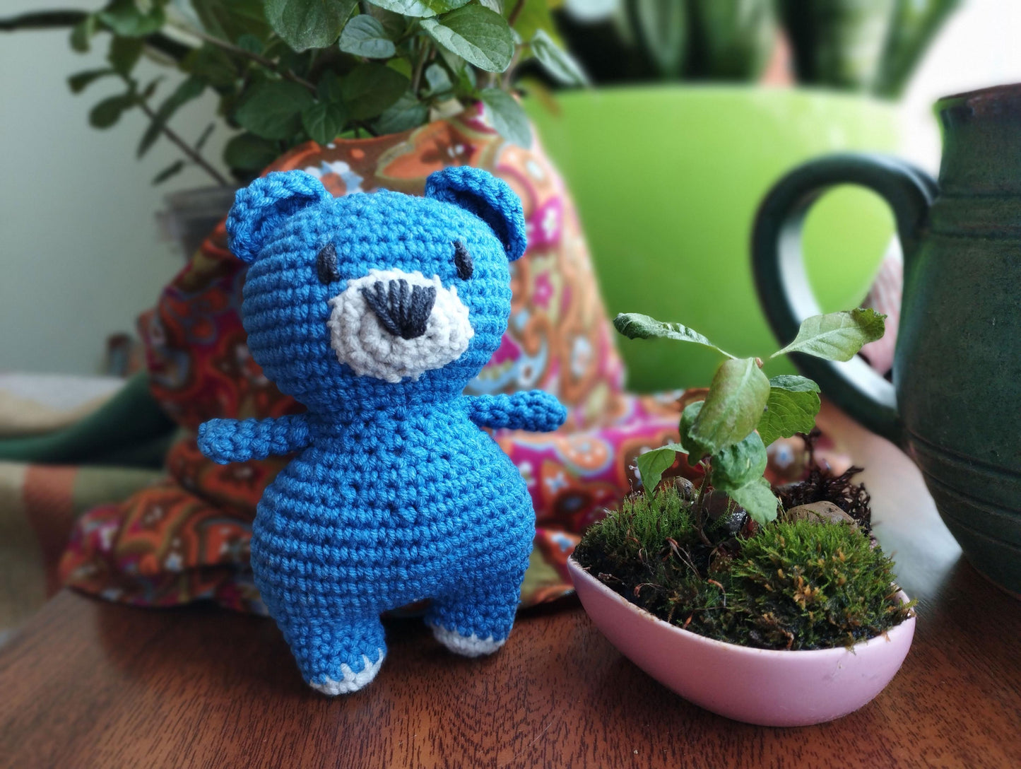 a crocheted blue teddy bear next to a potted plant