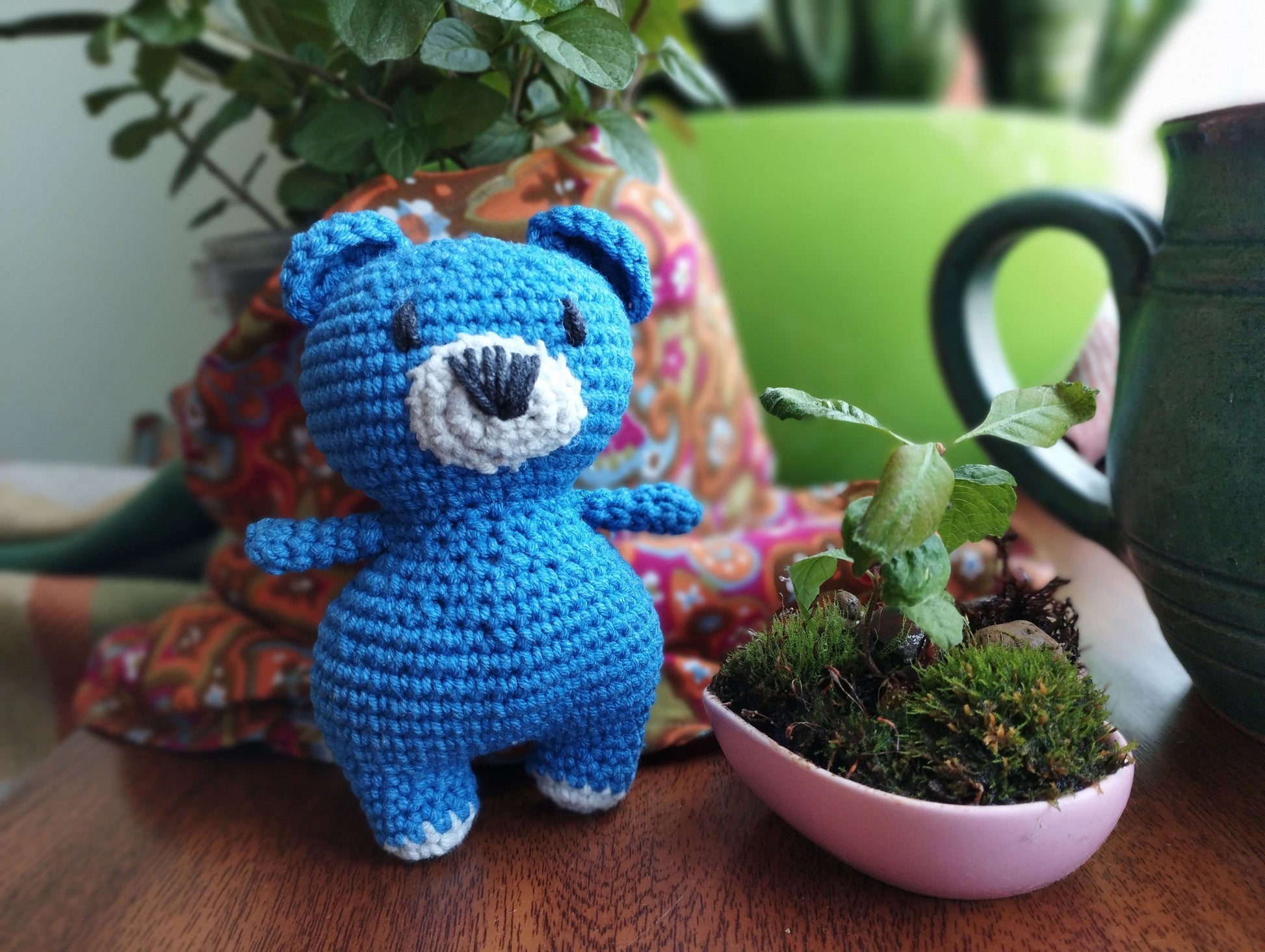 a crocheted blue teddy bear next to a potted plant