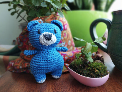 a crocheted blue teddy bear next to a potted plant