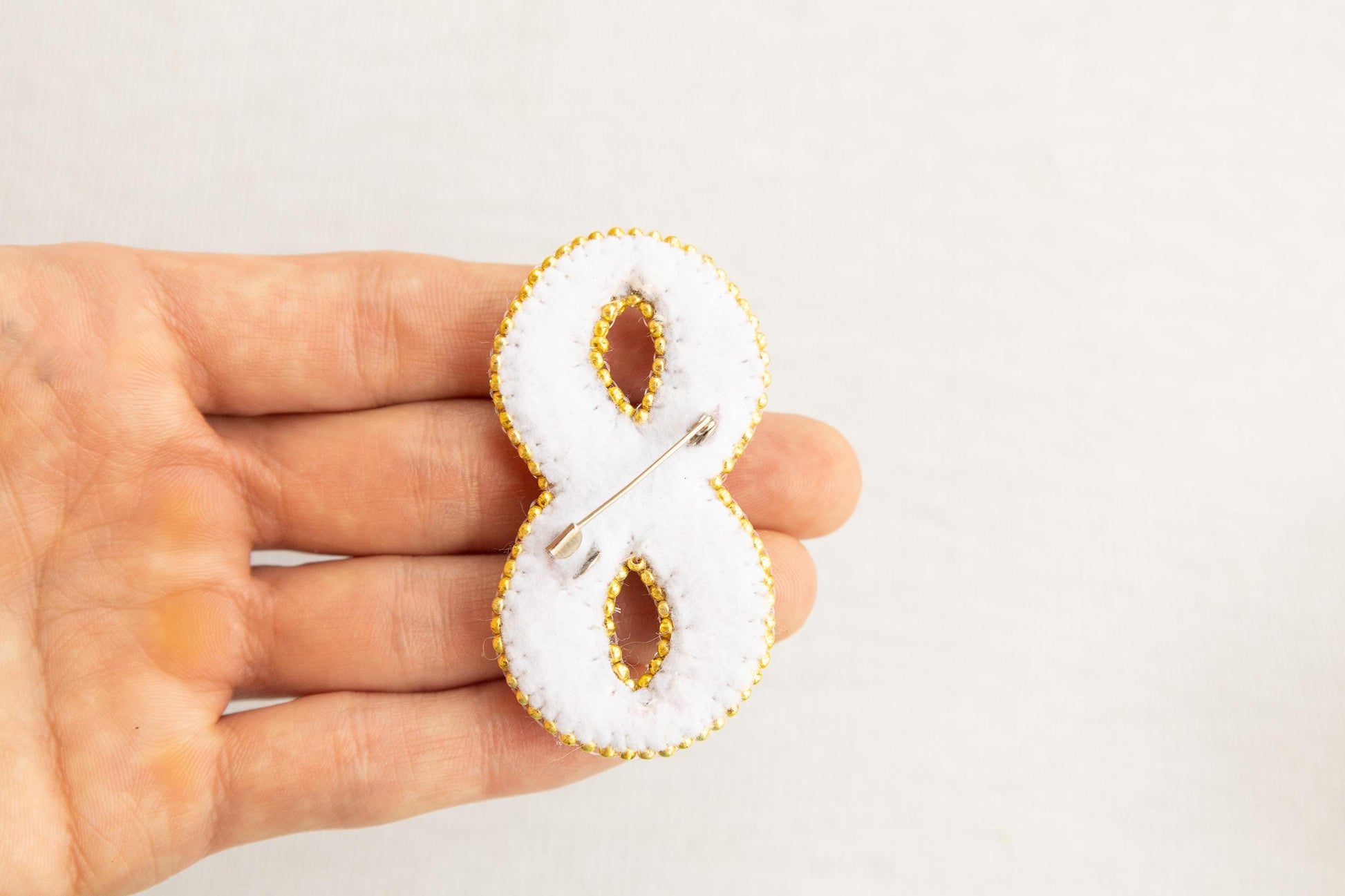 a hand holding a white and gold brooch