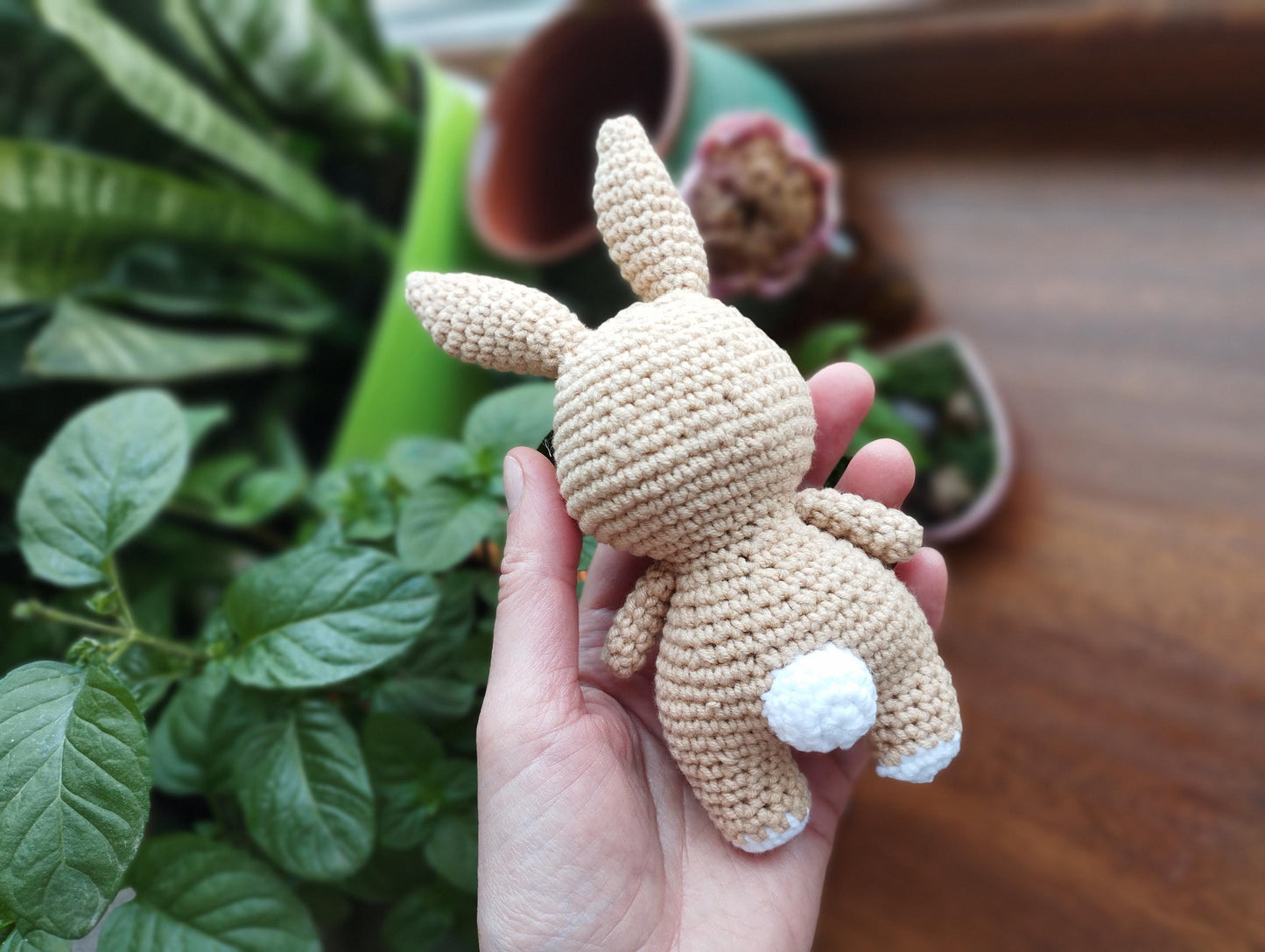 a hand holding a crocheted stuffed animal in front of a potted plant
