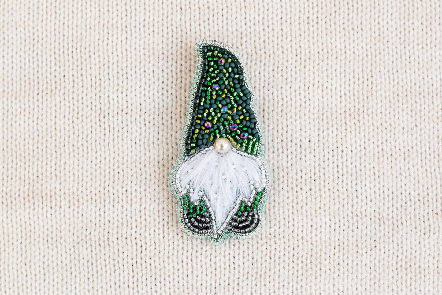 A decorative brooch in the shape of a gnome, made of colorful beads and a white beard.