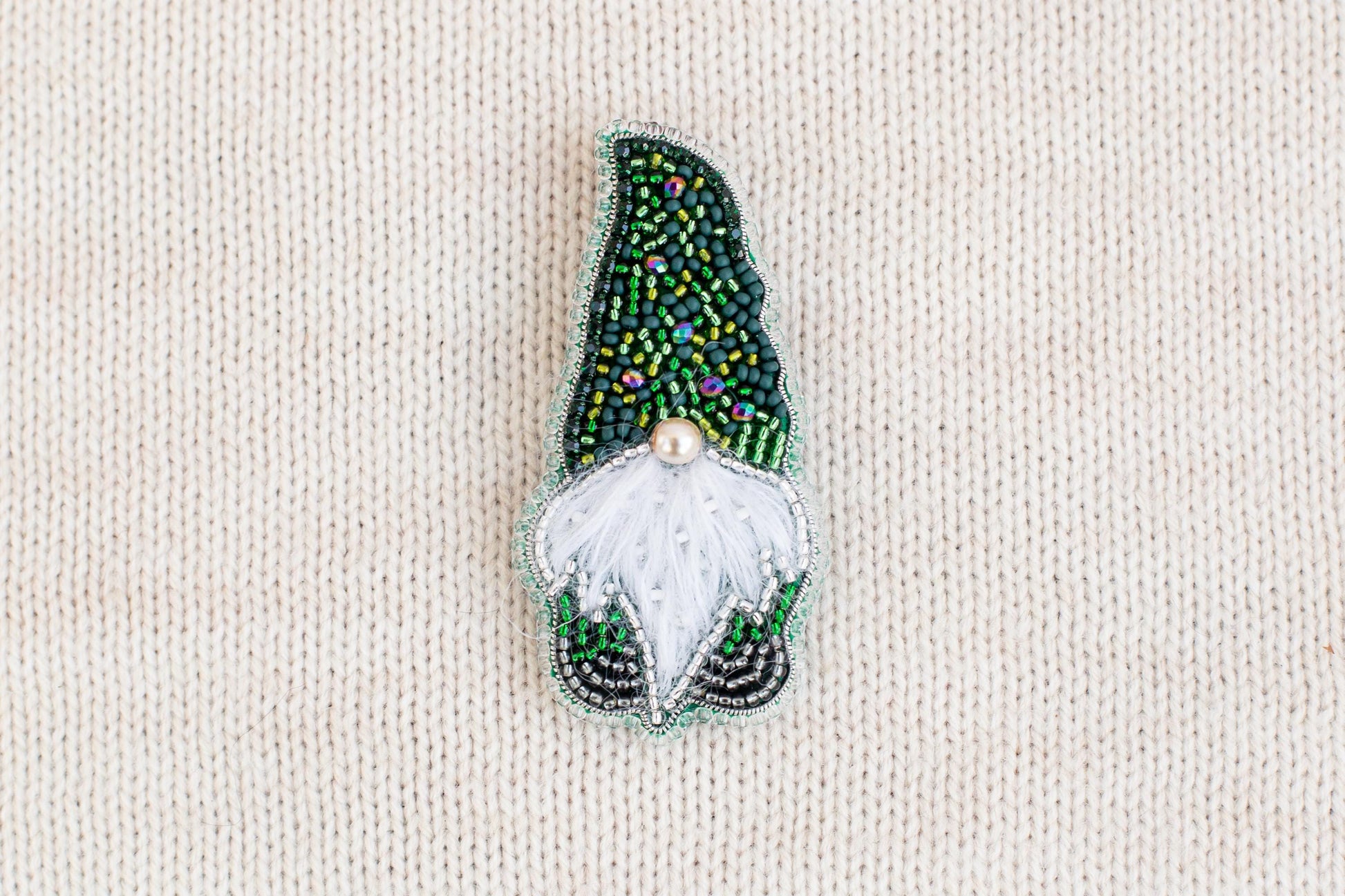 A decorative brooch in the shape of a gnome, made of colorful beads and a white beard.