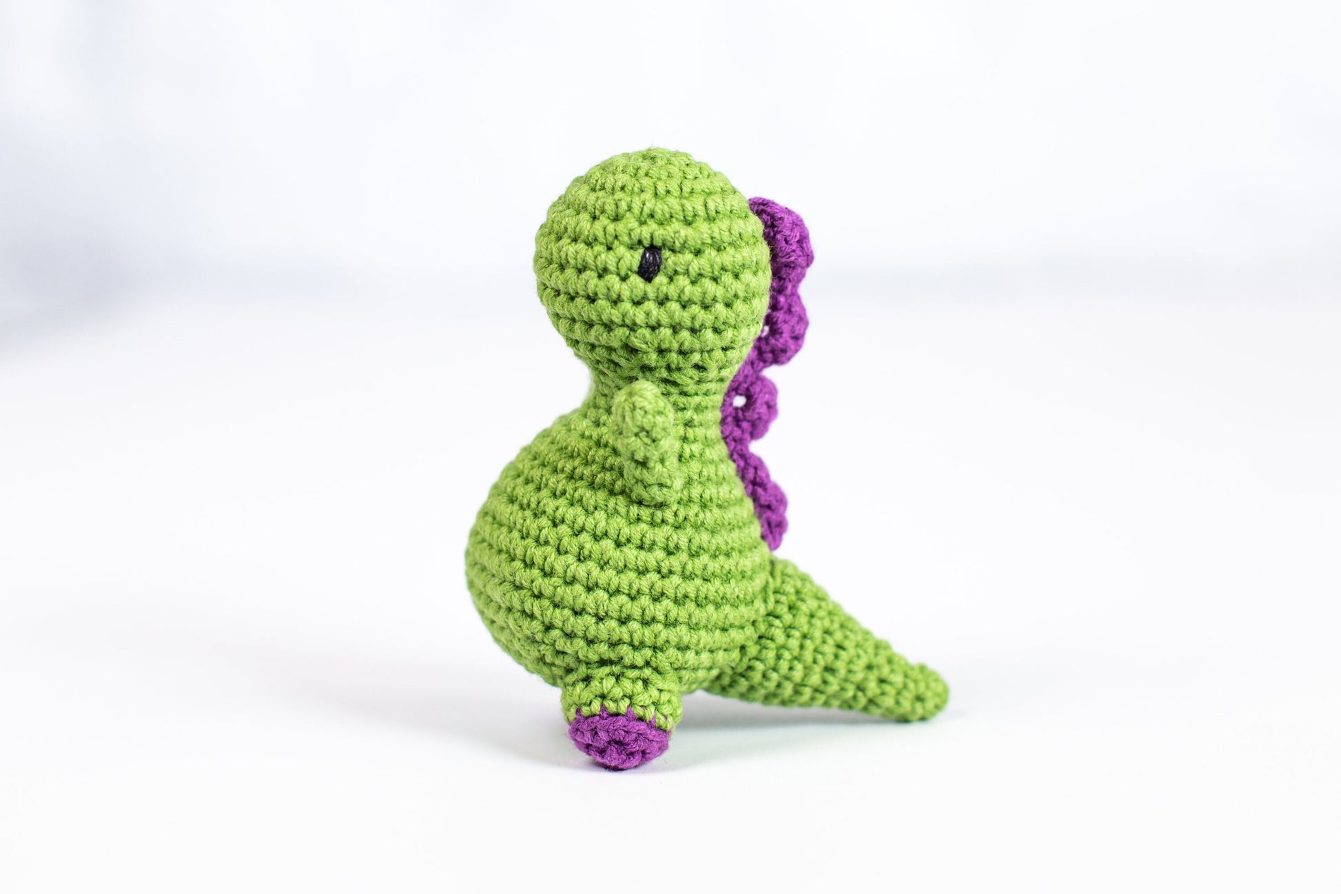 a crocheted green and purple toy sitting on a white surface