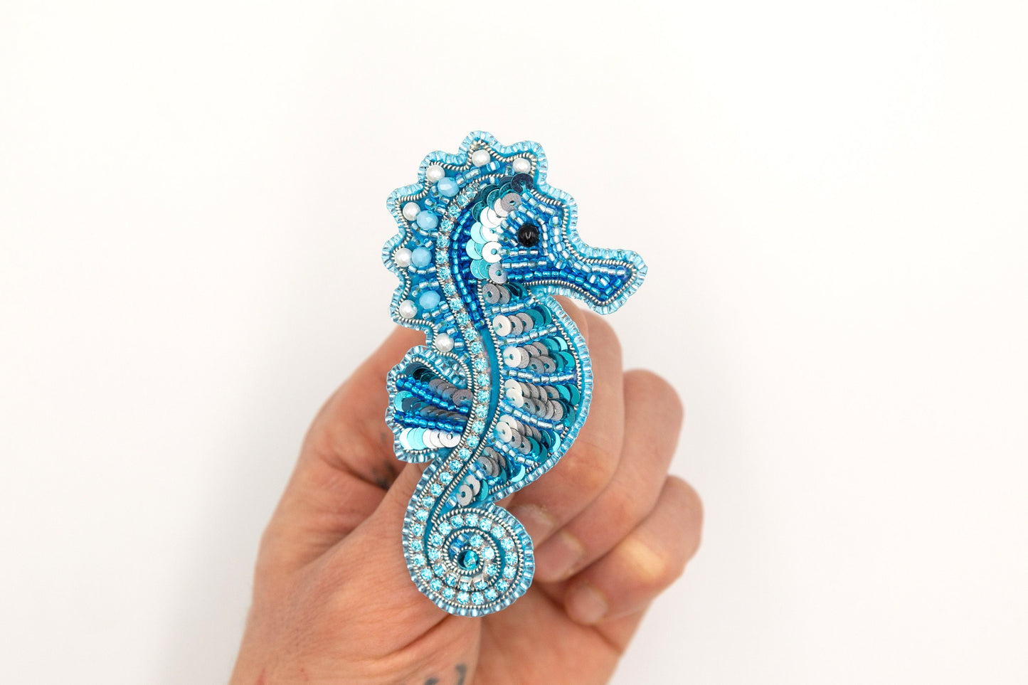 a hand holding a blue seahorse brooch
