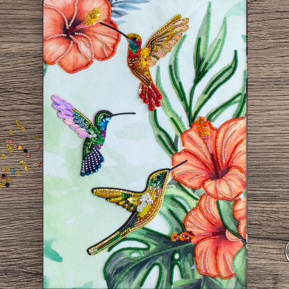 three colorful hummingbirds with beaks, surrounded by vibrant flowers and lush green leaves.