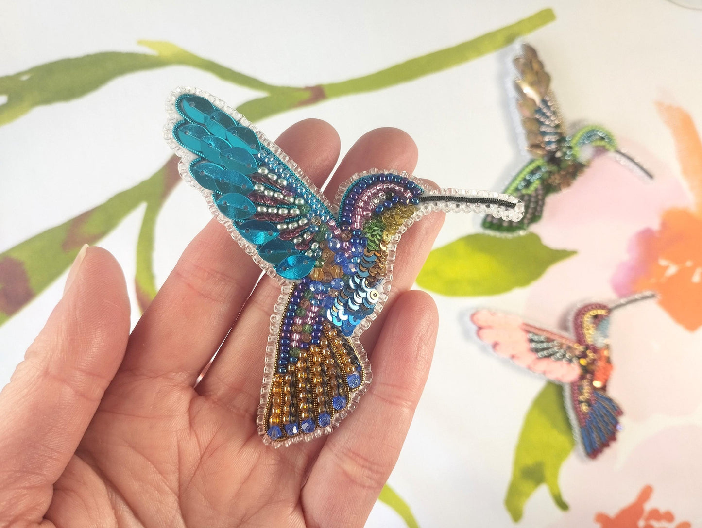 a hand holding a small beaded hummingbird brooch