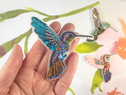 a hand holding a small beaded hummingbird brooch