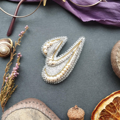 a variety of objects, including a decorative piece with pearls and a metallic design, a pair of glasses, a small acorn, a slice of orange, and some dried flowers.