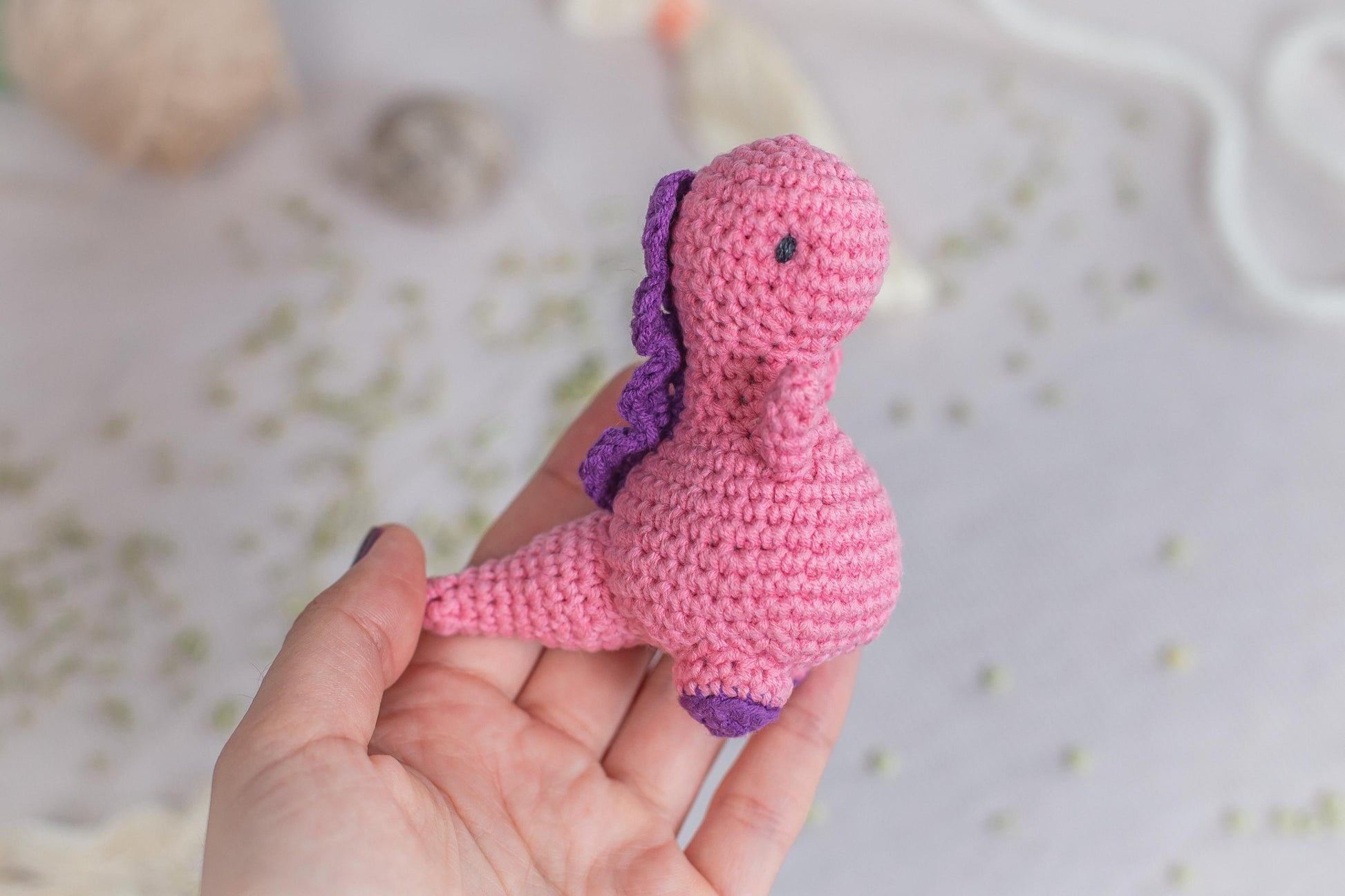 a hand holding a tiny pink crocheted toy