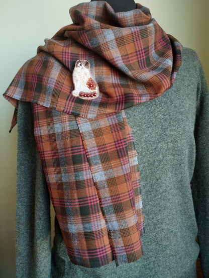 A plaid scarf with a cat embroidered on it, worn around a person's neck.