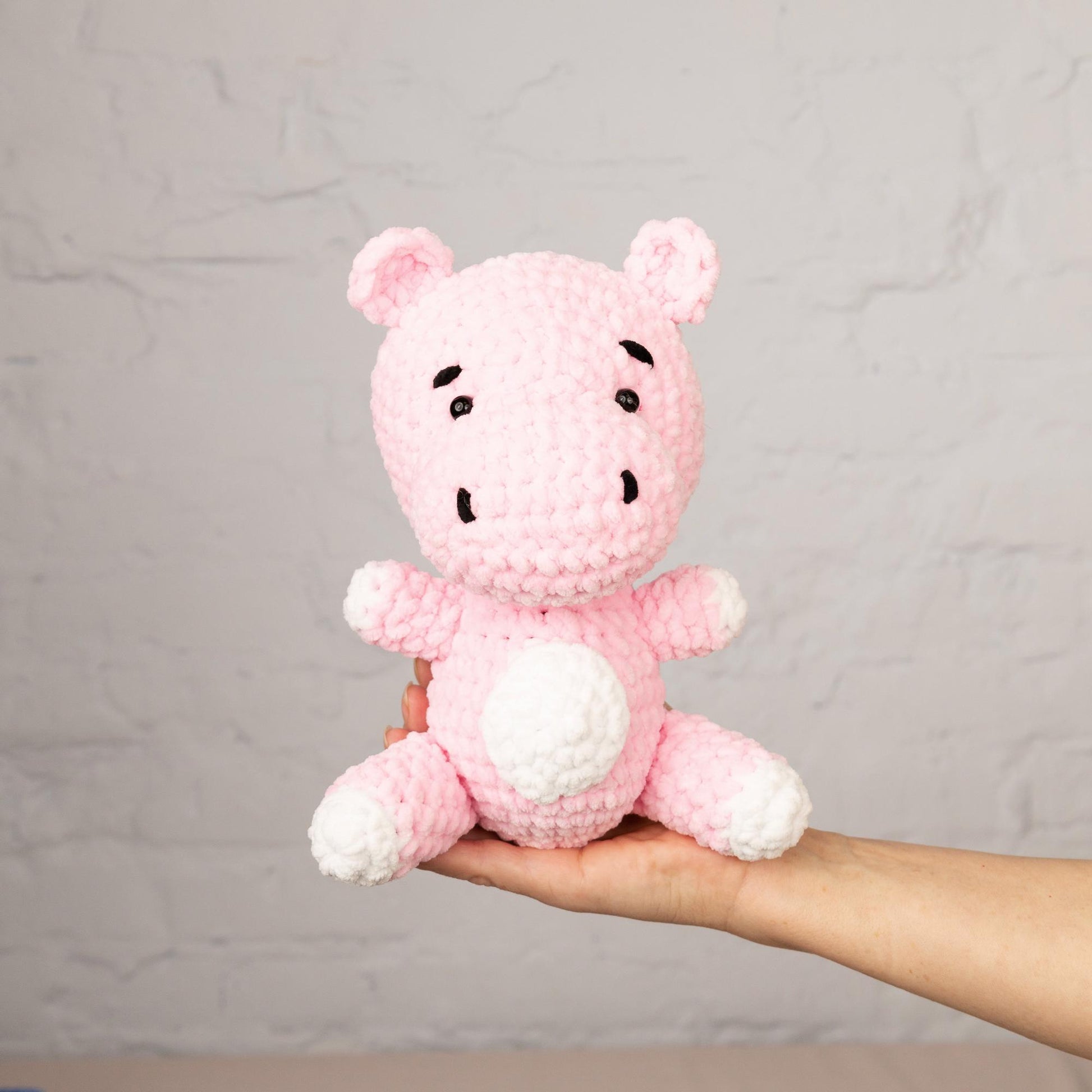 a hand holding a small pink crocheted teddy bear