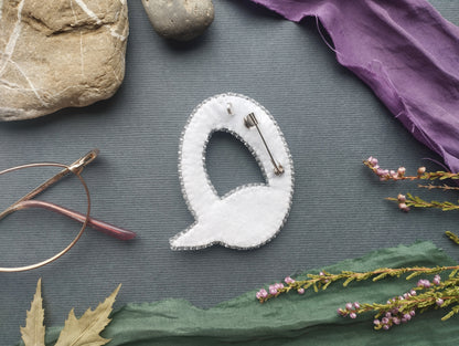 a close-up view of a white fabric object resembling a letter "Q" or a similar shape, surrounded by various objects such as a rock, a pair of glasses, and some flowers.