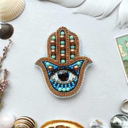 a handcrafted piece of jewelry with a blue and gold design, surrounded by various natural elements such as seashells, feathers, and a piece of paper.