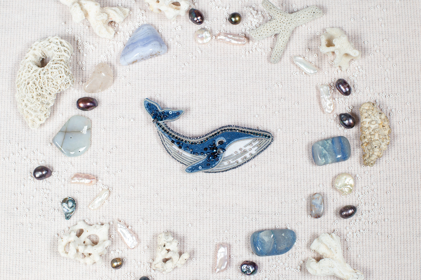 a collection of various natural elements, including a blue whale, pearls, seashells, and coral, arranged in a circular pattern on a light-colored background.