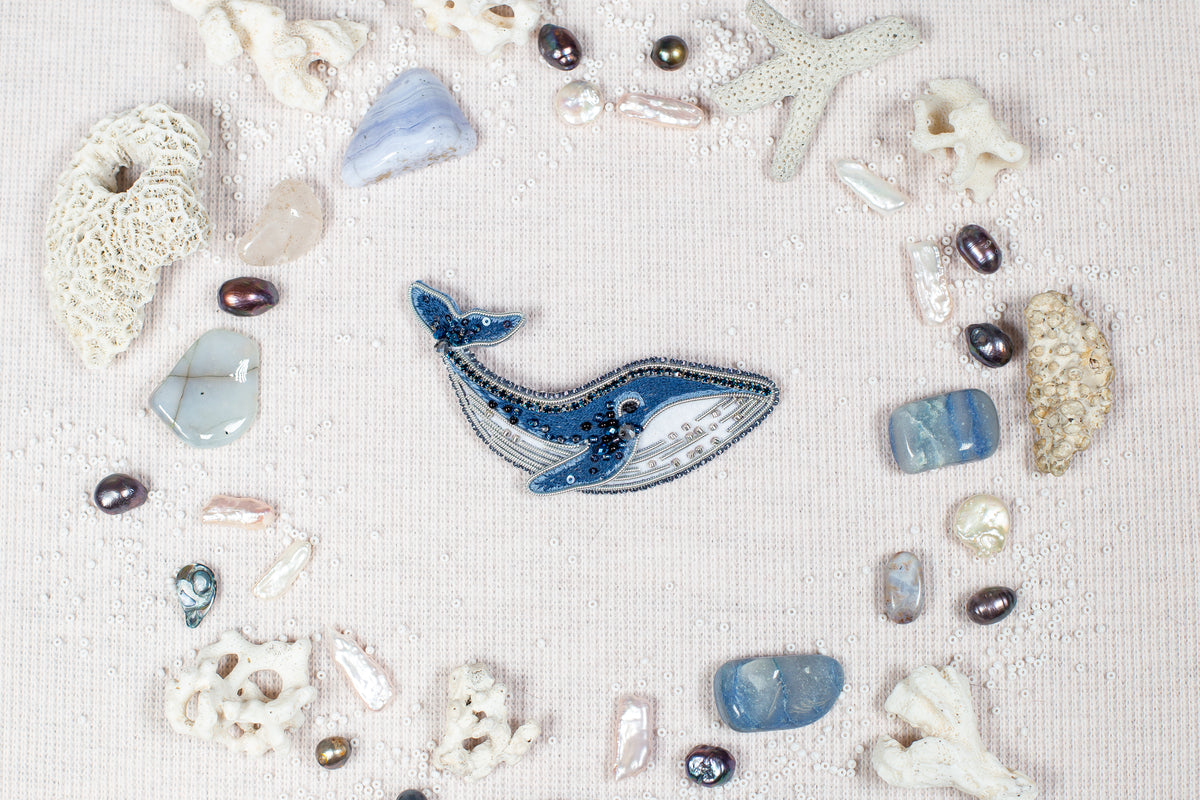a collection of various natural elements, including a blue whale, pearls, seashells, and coral, arranged in a circular pattern on a light-colored background.