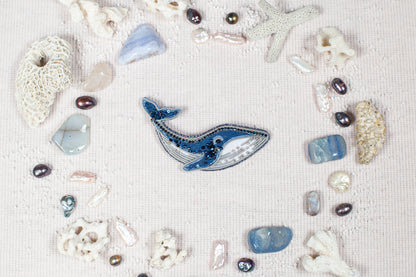 a collection of various natural elements, including a blue whale, pearls, seashells, and coral, arranged in a circular pattern on a light-colored background.