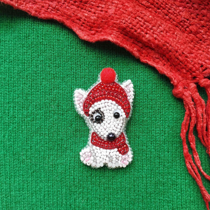 A small, white dog-shaped pin made of beads and a red hat is displayed against a green background, with a red scarf visible on the right side.