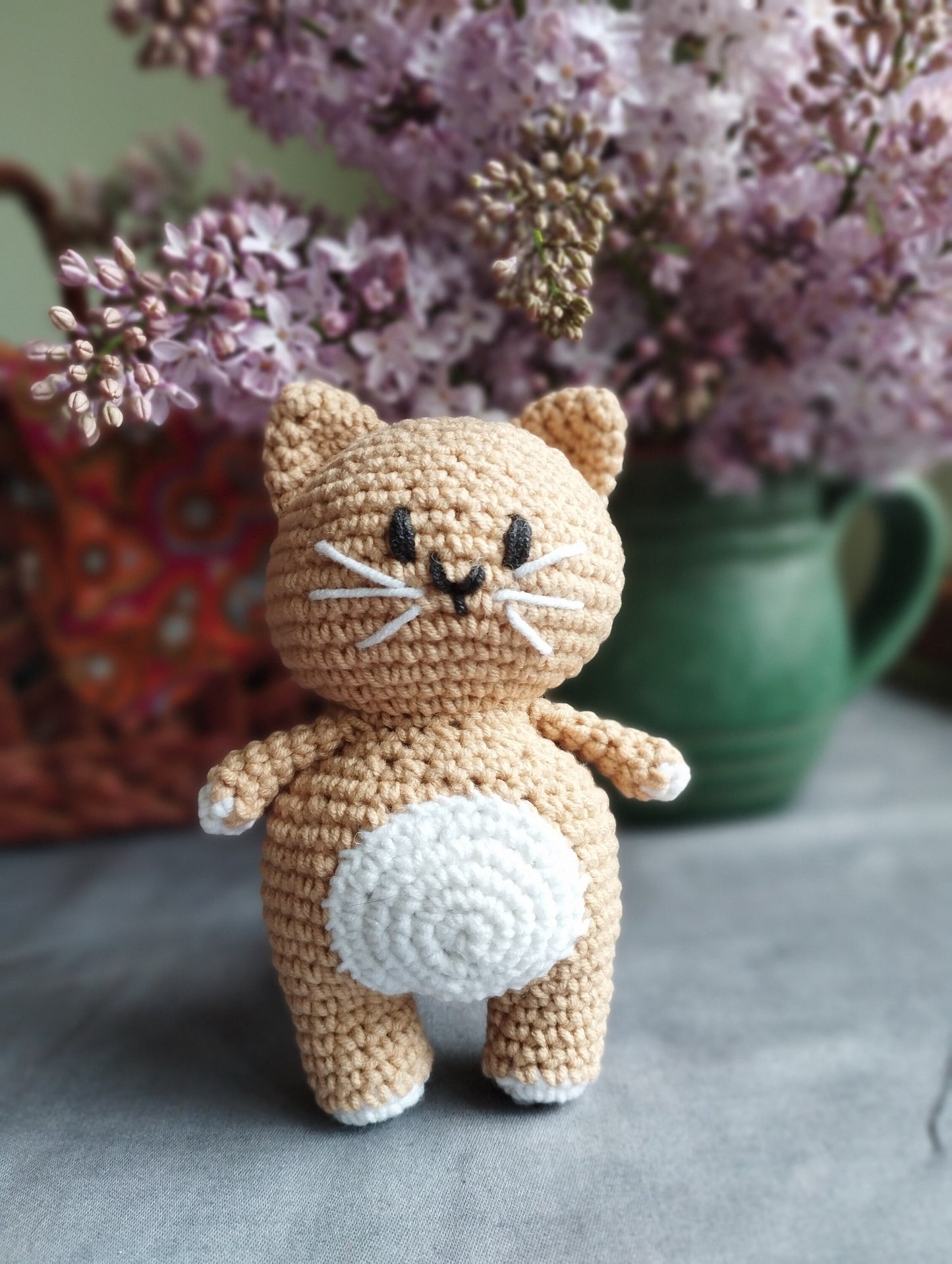 a crocheted cat sitting on a table next to a vase of flowers