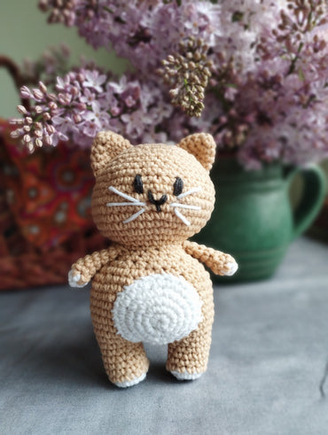 a crocheted cat sitting on a table next to a vase of flowers