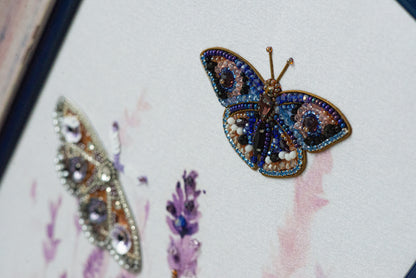 two butterflies, one with a blue and gold design and the other with a purple and gold design, both adorned with intricate beading and embroidery.