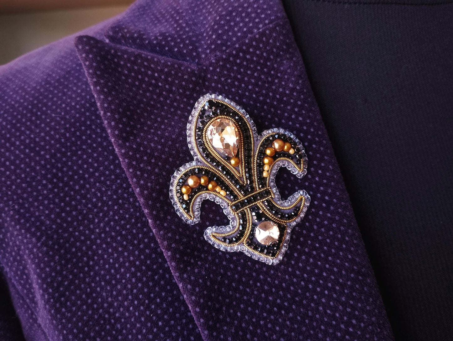 A close-up view of a purple jacket with a decorative fleur-de-lis brooch on the lapel.
