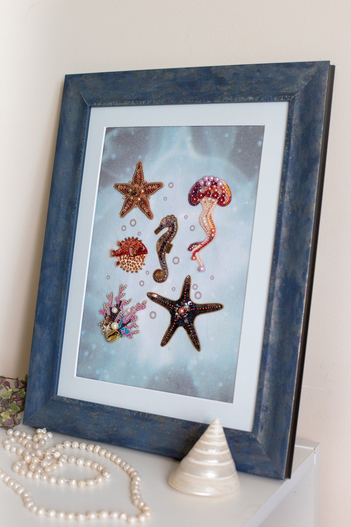 a framed artwork of various sea creatures, including a starfish, a jellyfish, and a seahorse, set against a blue background.