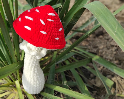 a red and white knitted mushroom sitting in the grass