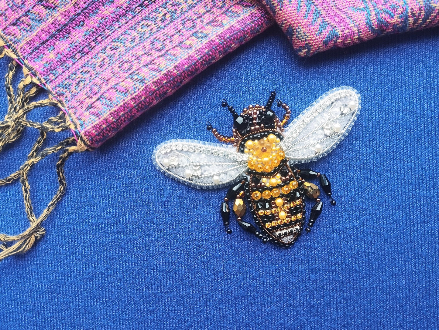 A close-up view of a beaded, embroidered bee pin on a blue fabric surface.