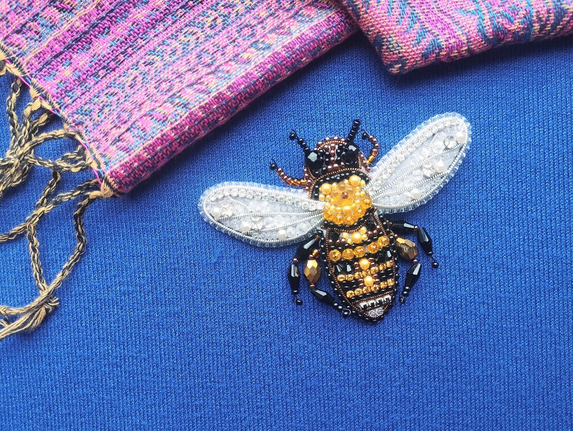 A close-up view of a beaded, embroidered bee pin on a blue fabric surface.
