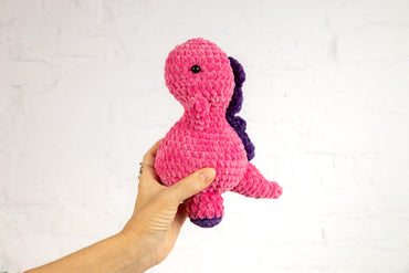 a hand holding a pink and purple stuffed animal