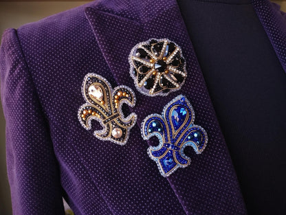 A close-up view of a purple jacket with three decorative brooches or pins attached to the lapel.